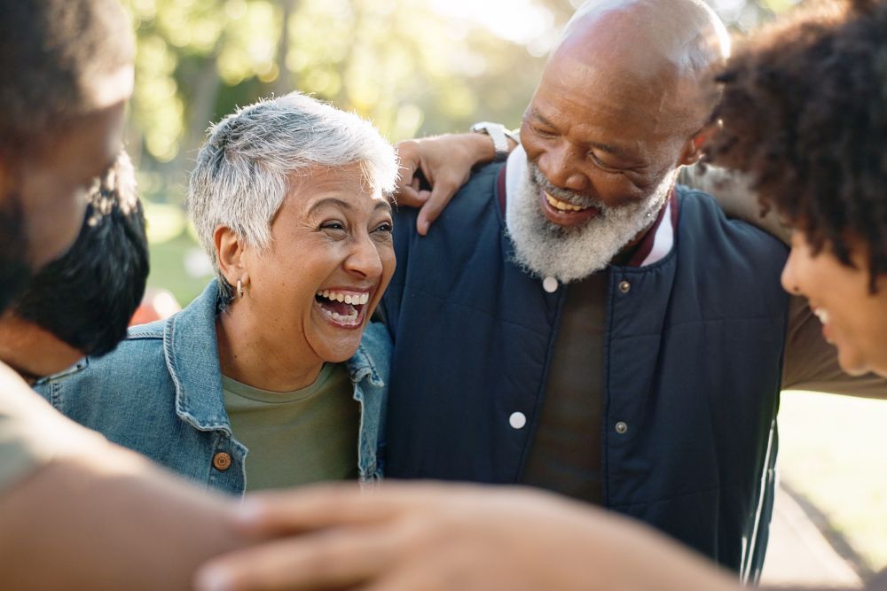 Group of adults standing outdoors, smiling and laughing together, showing joy, connection, and community.