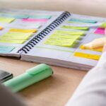 Person highlighting tasks in a colorful planner filled with sticky notes, creating an organized daily routine on a desk with a highlighter and smartphone nearby.