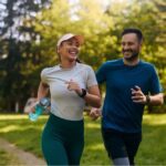 Man and woman jogging together through a sunlit park, smiling and enjoying the moment, symbolizing the physical and emotional benefits of exercise.