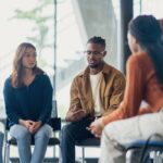 Diverse group of people sitting in a circle during a group therapy session, listening and sharing in a supportive environment.