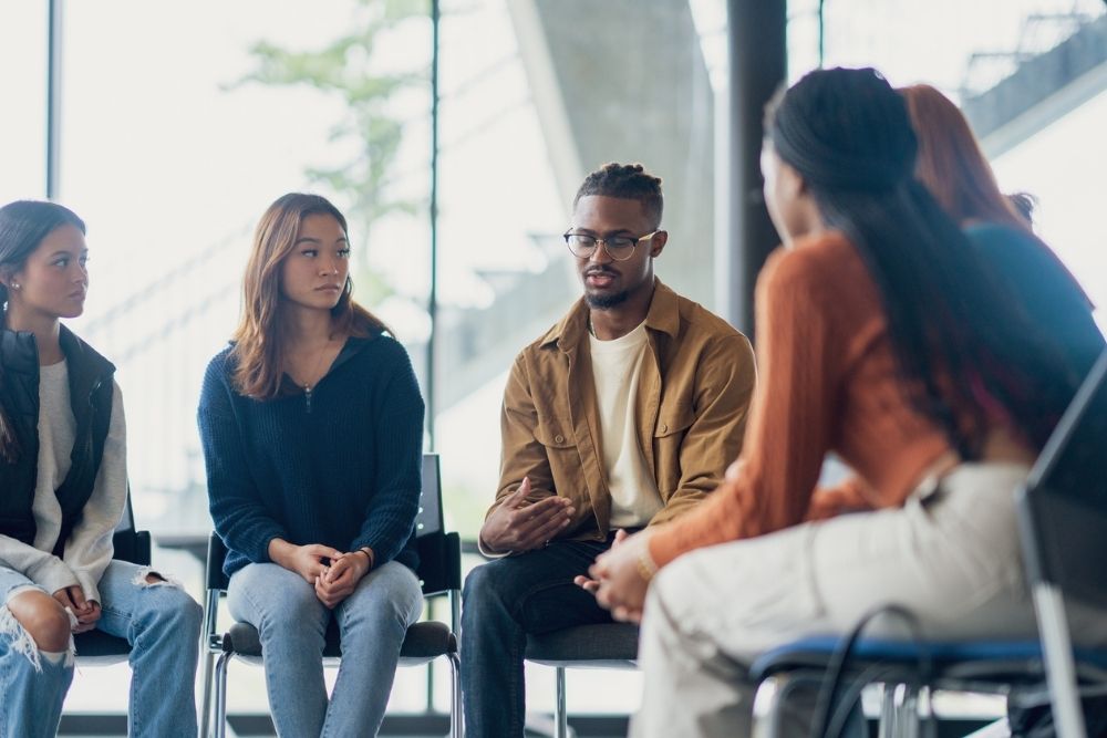 Diverse group of people sitting in a circle during a group therapy session, listening and sharing in a supportive environment.
