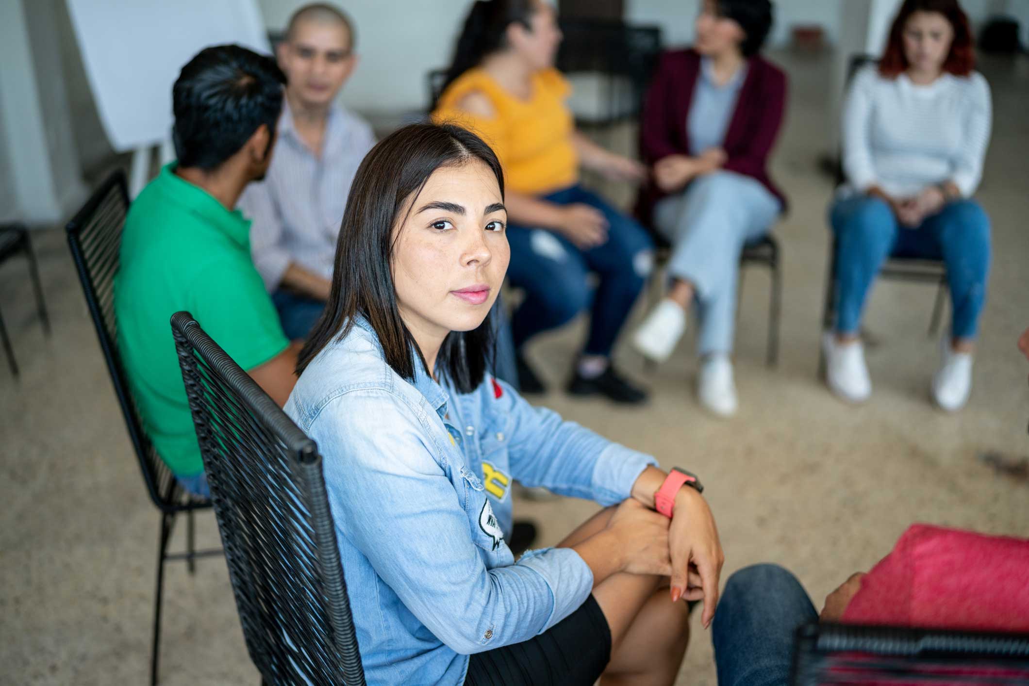 Diverse group of people sitting in a circle during a group therapy session, listening and sharing in a supportive environment.