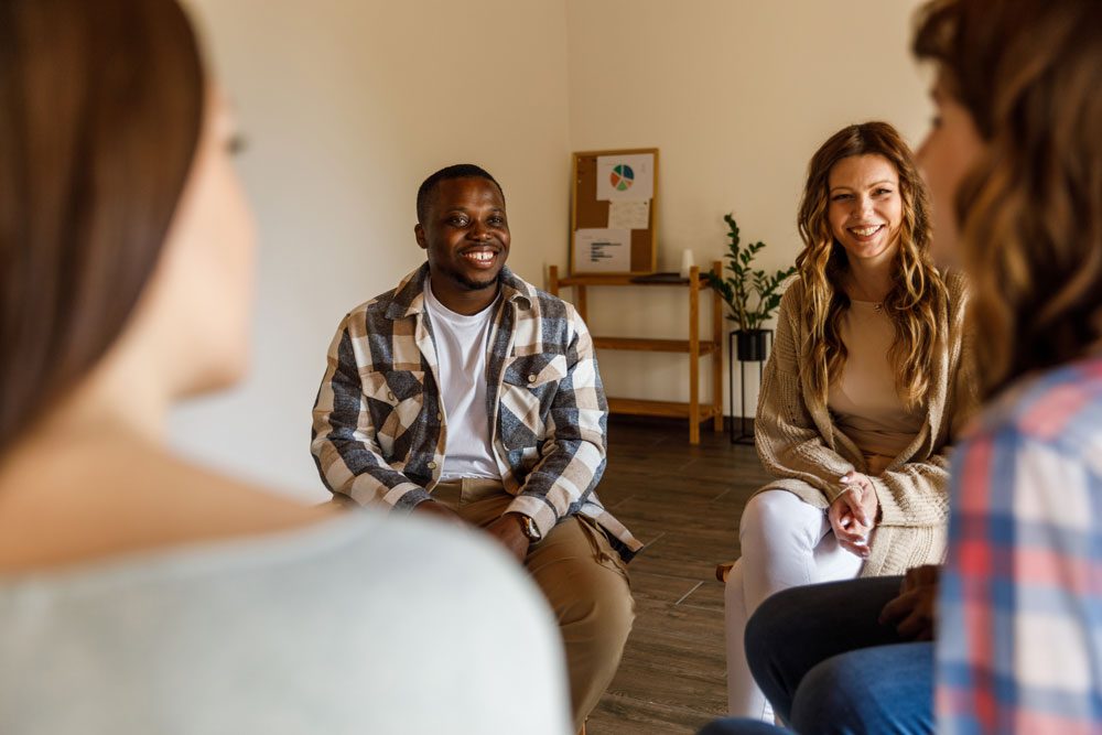 Diverse group of people sitting in a circle during a group therapy session, listening and sharing in a supportive environment. Intensive Outpatient Program IOP - Partial Hospitalization Program - PHP