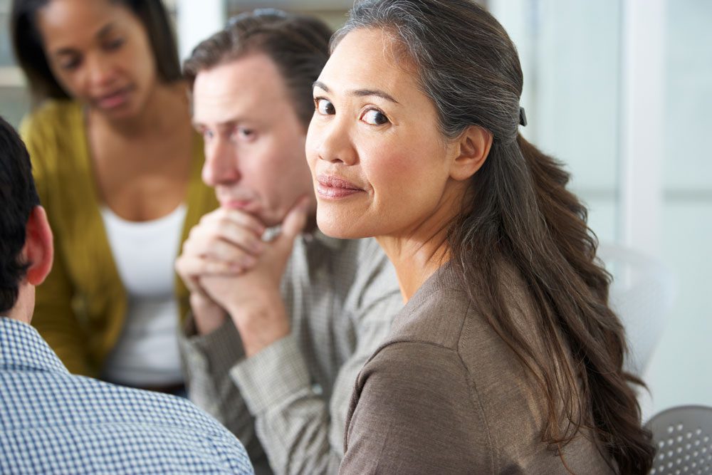 Diverse group of people sitting in a circle during a group therapy session with one looking back at the camera, listening and sharing in a supportive environment. Intensive Outpatient Program IOP - Partial Hospitalization Program - PHP