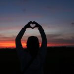 silhouette of a person holding up their hands in the shape of a heart with a beautiful sunset in the background