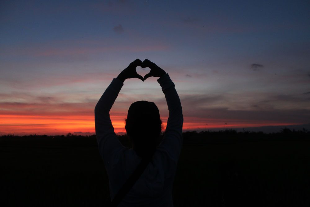 silhouette of a person holding up their hands in the shape of a heart with a beautiful sunset in the background
